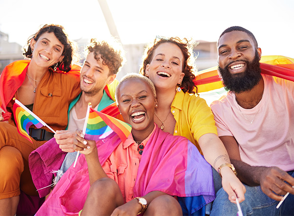 Group of diverse friends wearing bright colors and smiles, with LGBTQ flags.