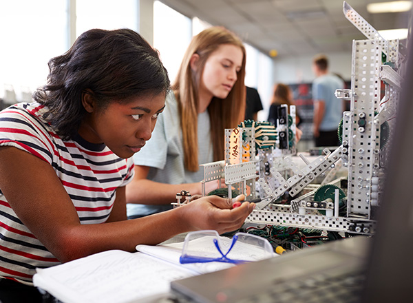 Two young female students working on a robotics project together.