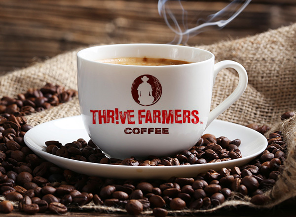 White coffee mug that reads Thrive Farmers Coffee surrounded by coffee beans.