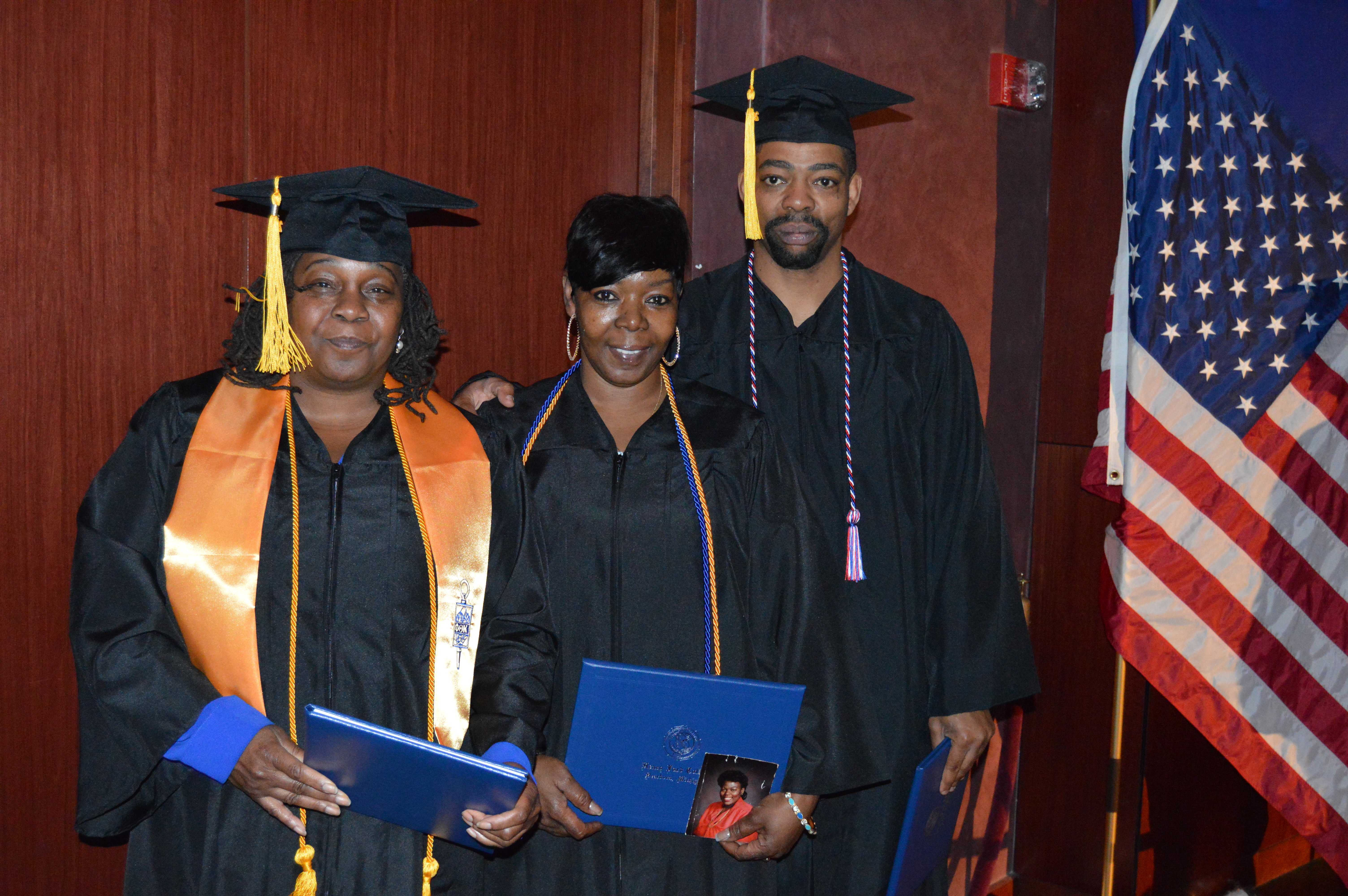 From left to right: Brenda McCall, Beverly Etchen and Carl Matsey II stand in graduation gowns and caps holding diplomas
