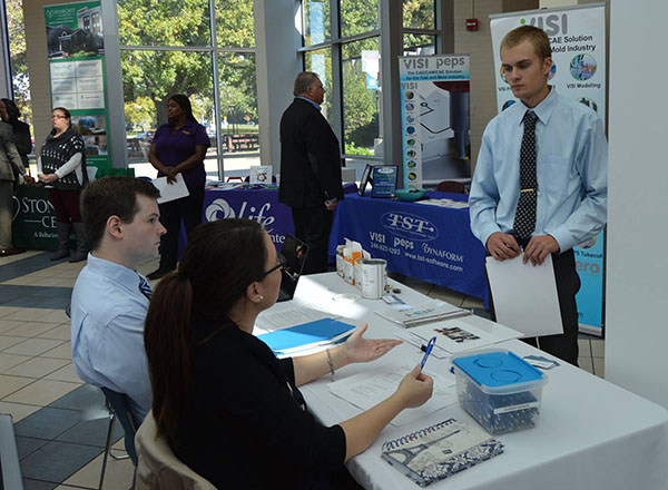 Employer speaking to two students at a table at an HFC career fair