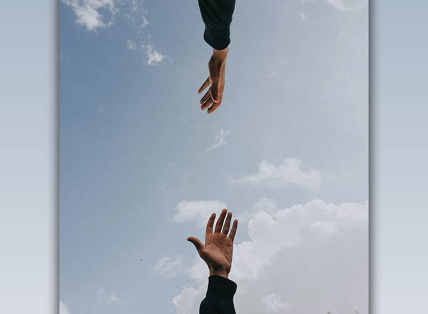An image of two hands reaching toward each other with the sky in the background.