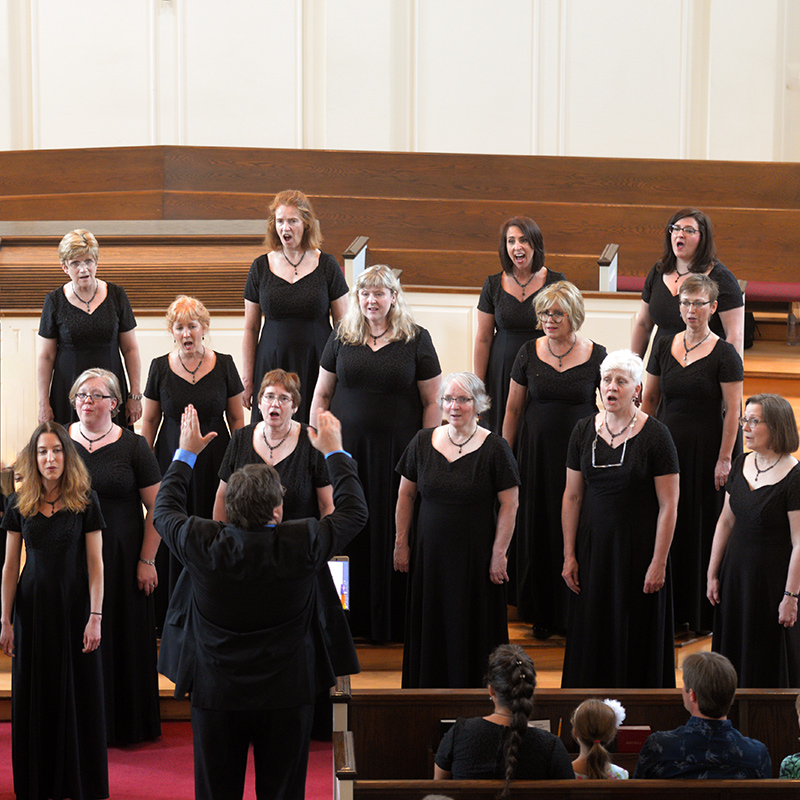 Women in black choral robes performing on staircase of renaissance-style building