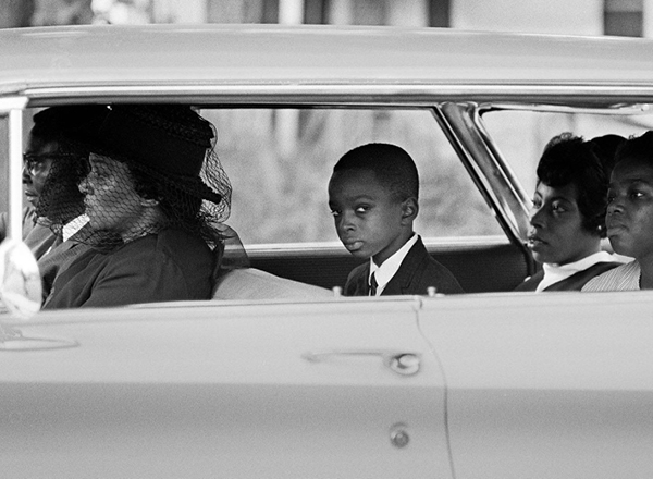 A young black boy riding in a car with his family in the 1960s. 