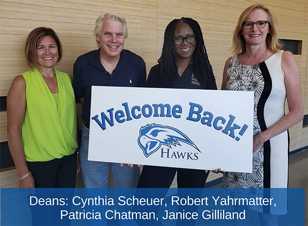 HFC's four school deans holding a Welcome Back Hawks poster