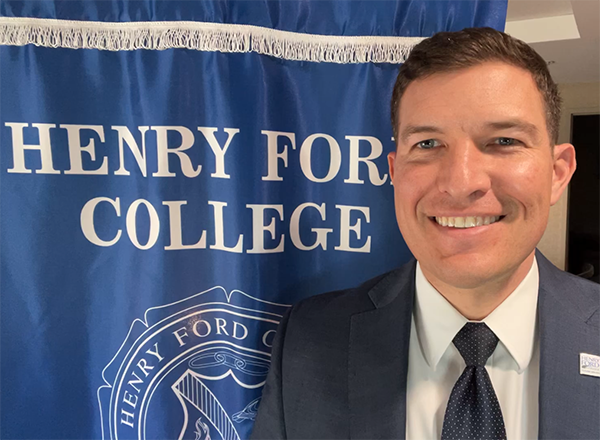 Russ Kavalhuna in front of Henry Ford College banner