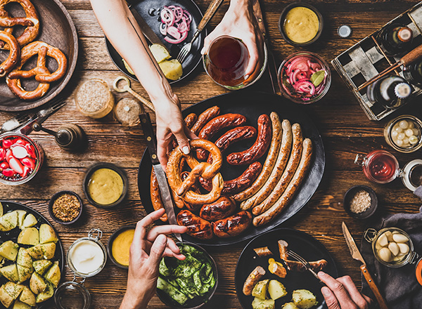 A table shot from above of Oktoberfest food such as bratwurst and knackwurst, German potatoes, and pretzels.