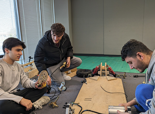 Three engineering students in a classroom sitting on the ground working on an engineering project together.