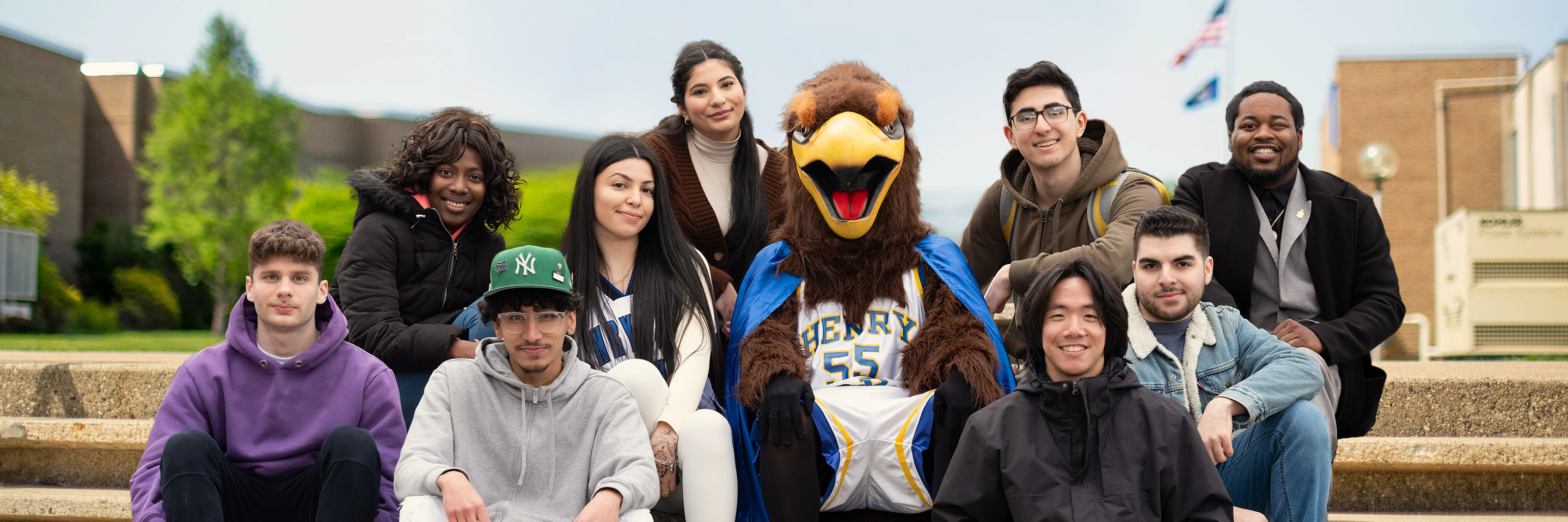 Students on Henry Ford College campus, sitting outside on a set of stairs with the HFC mascot "Hawkster"