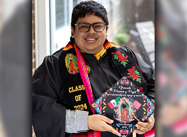 Jesus Cruz-Navarro, smiling and holding his decorated graduation cap.