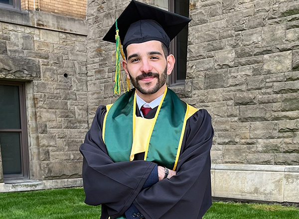 Mohammad Turaani is smiling at camera wearing his Wayne State University cap and gown.