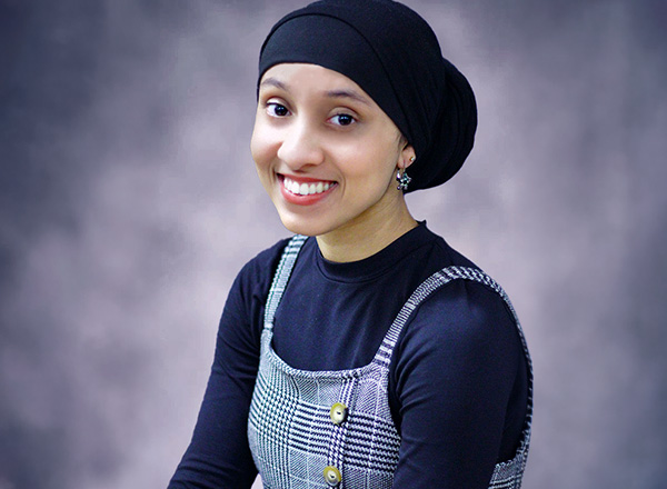 Nyla Abdulla is wearing a dark navy headscarf, with a dark navy long sleeved shirt and patterned jumper. 