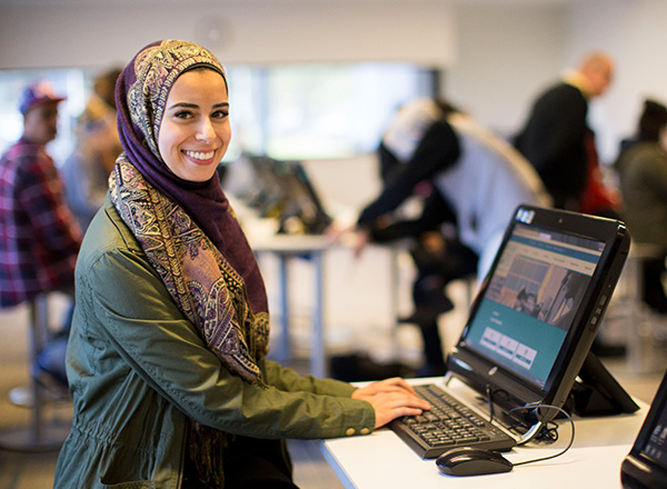 A woman in a hijab smiling and using the computer in the Welcome Center.