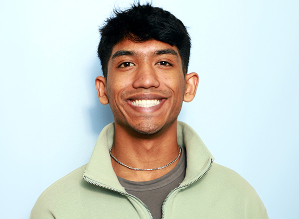 Sabit Islam has dark hair, smiling, wearing a light green pullover. 