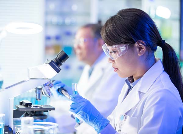 A women weaing gloves working with a microscope.