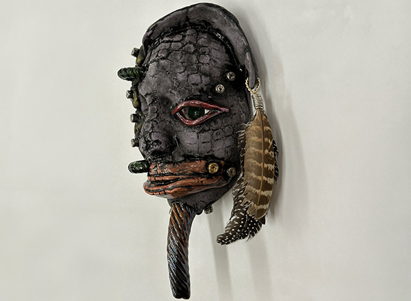 One of Steve Glazers ceramic mask, from his collection called "Motor City Griots". Painted in moody dark colors with a feather.