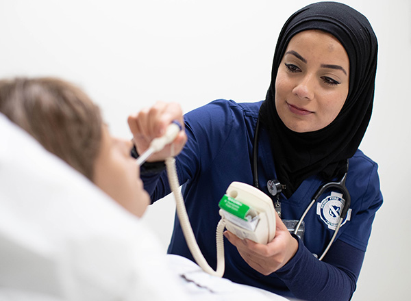 Female nursing student wearing a hijab and scrubs, tending to a nursing patient mannequin.