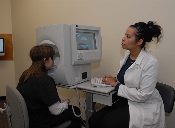 A female sitting at a computer with a patient getting her eyes checked.