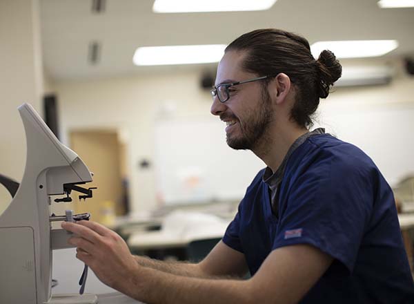 A male ophthalmic technician looking at a pair of glasses under a microscope.