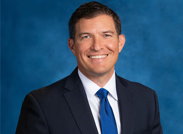 President Russ Kavalhuna's headshot. He is smiling and wearing a dark suit with blue tie in front of a blue backdrop.