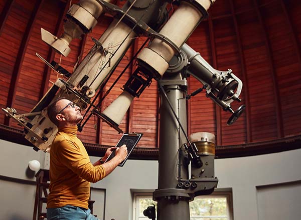 A man looking at a screen while standing by a telescope.