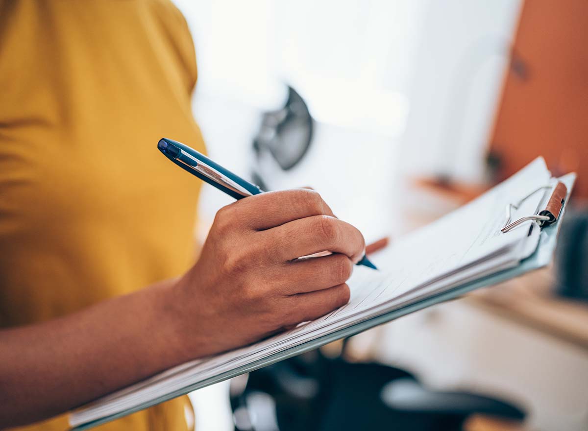 A close up of a woman writing on paper on a clipboard.