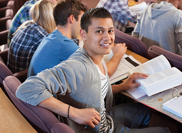 Young male student in a college classroom looking over his shoulder to the camera.