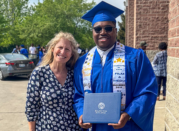 Susan McGraw(left) is wearing a floral dress and posing next to Tyrone Bean(right) who is wearing HFC graduation cap and gown, holding his diploma.