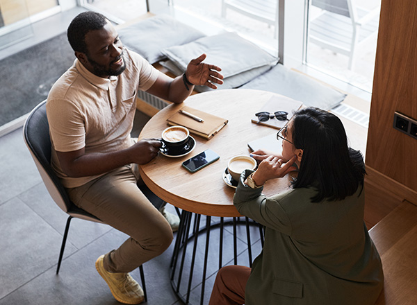 High angle portrait of two young people chatting at table and drinking coffee.