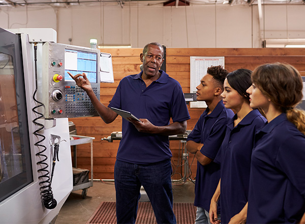 Engineer training apprentices on CNC machine.