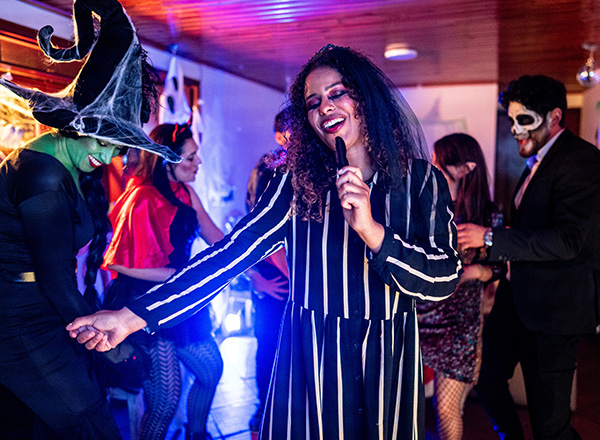 Woman dancing and singing karaoke with friends at a Halloween party.