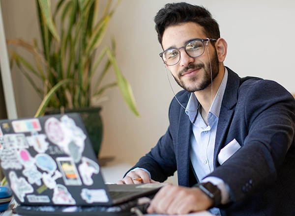 Mohammad Turaani is smiling, sitting at a table with his laptop open.