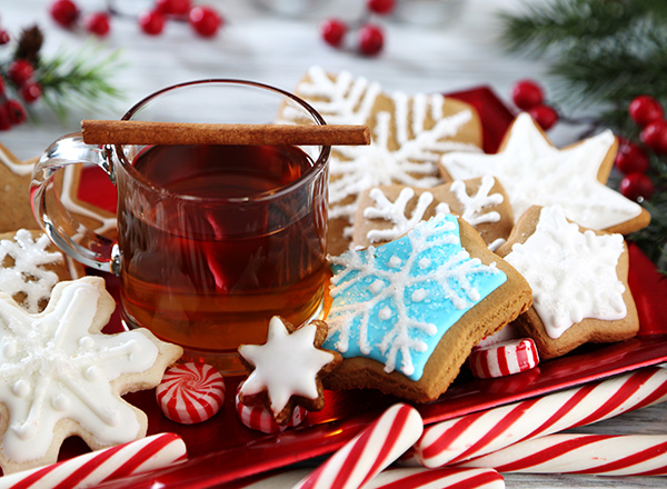 Clear mug of spiced cider on a tray surrounded by decorated cookies and candy cane sticks.