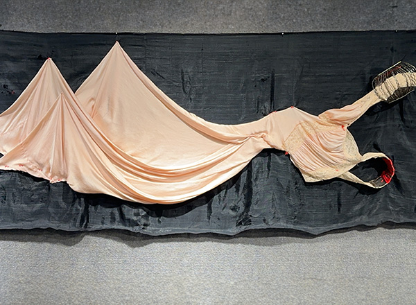 Fabric wall art made up pf a peach colored dress on a dark charcoal fabric background.