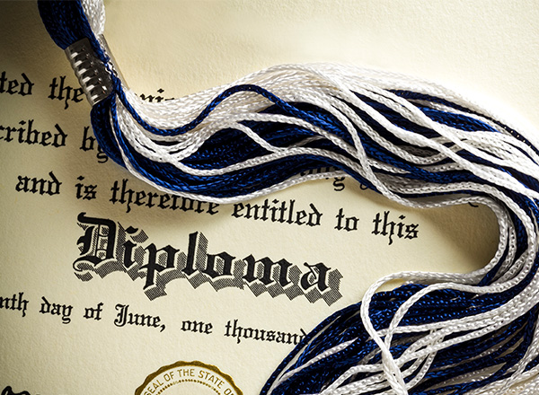 A closeup of a graduation cap tassel and diploma.