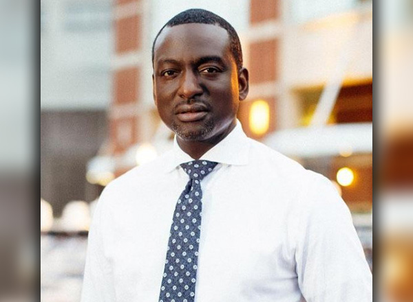 Dr. Yusef Salaam is wearing a white button down shirt and blue and white dotted tie. 