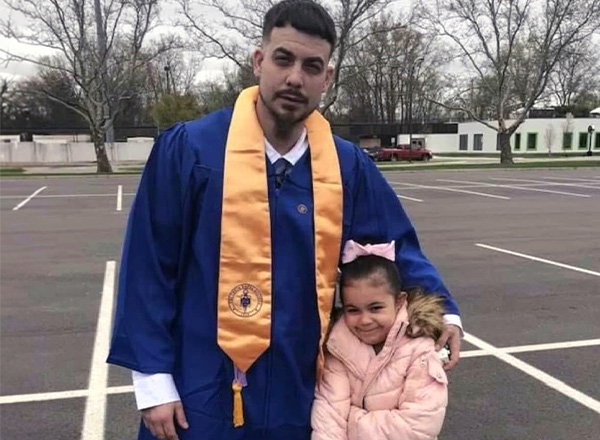 Joshua Ragland is wearing graduation gown and posing with his daughter. 