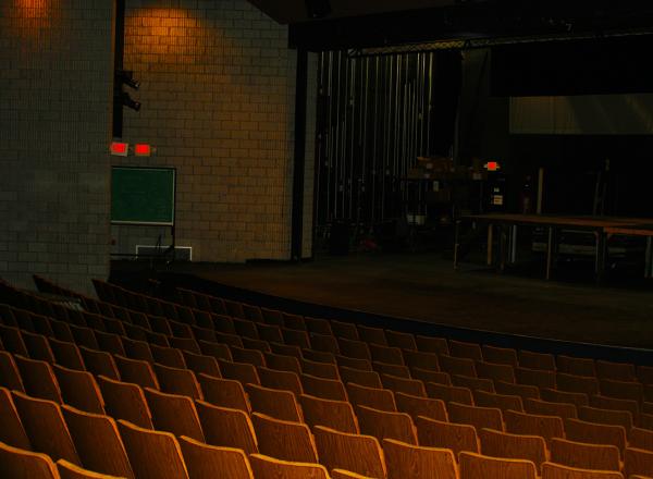 Photograph of inside of Adray Auditorium, with several rows of seats facing the stage that spans the width of the auditorium 